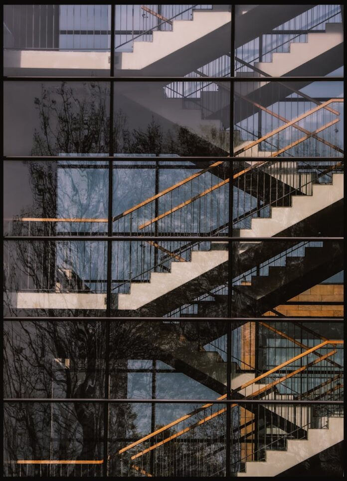 Reflection of trees and staircase in a glass facade showcasing modern architecture.
