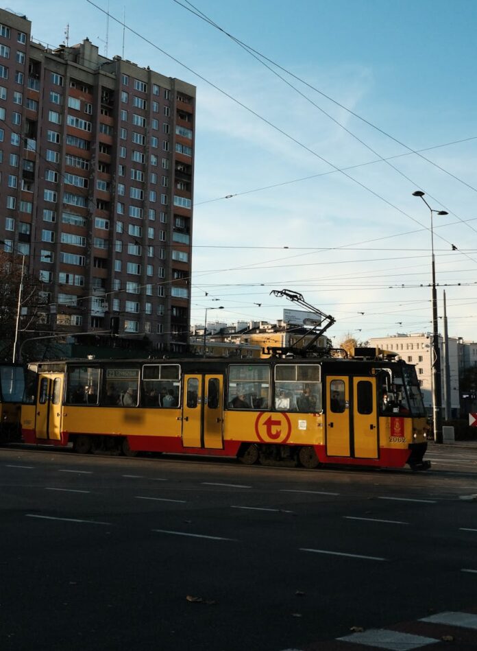 Yellow tram traverses through urban cityscape in Warsaw, emphasizing vibrant city life.